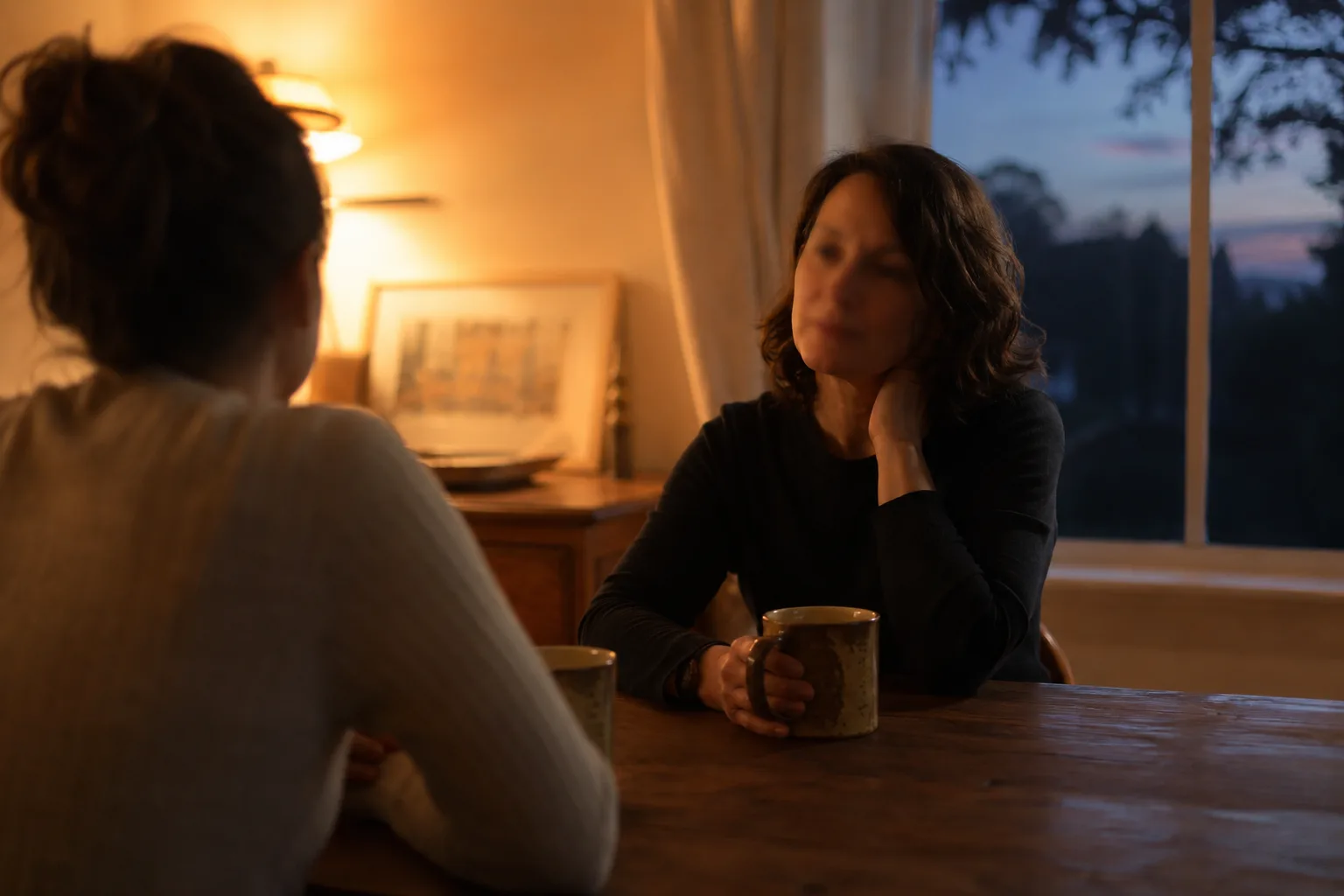 Two people having a warm, unhurried conversation over coffee at dusk